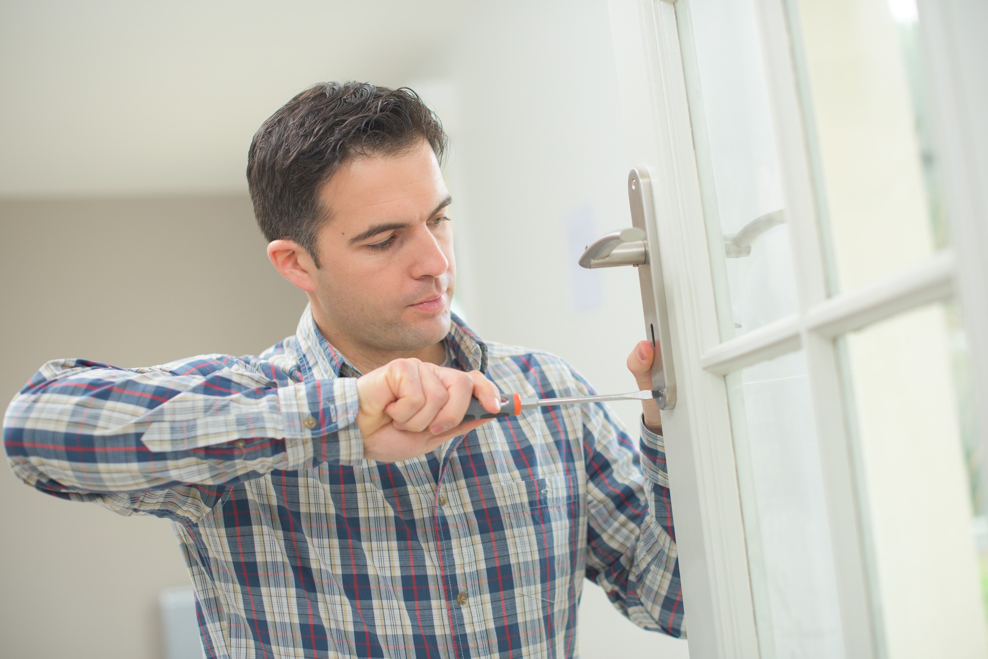 Man repairing a door handle with a screwdriver, demonstrating home maintenance skills in a well-lit interior setting.